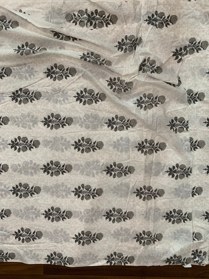 May include: White fabric with a repeating pattern of black floral sprigs. The fabric is folded and wrinkled.