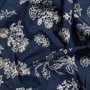 May include: A dark blue fabric with a white floral pattern. The fabric is textured and has a slightly wrinkled appearance.