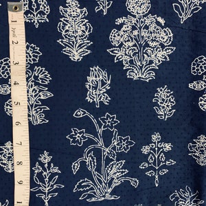 May include: A navy blue fabric with a white floral pattern. The fabric has a subtle dotted texture. The pattern features various floral motifs, including large and small flowers, leaves, and stems.