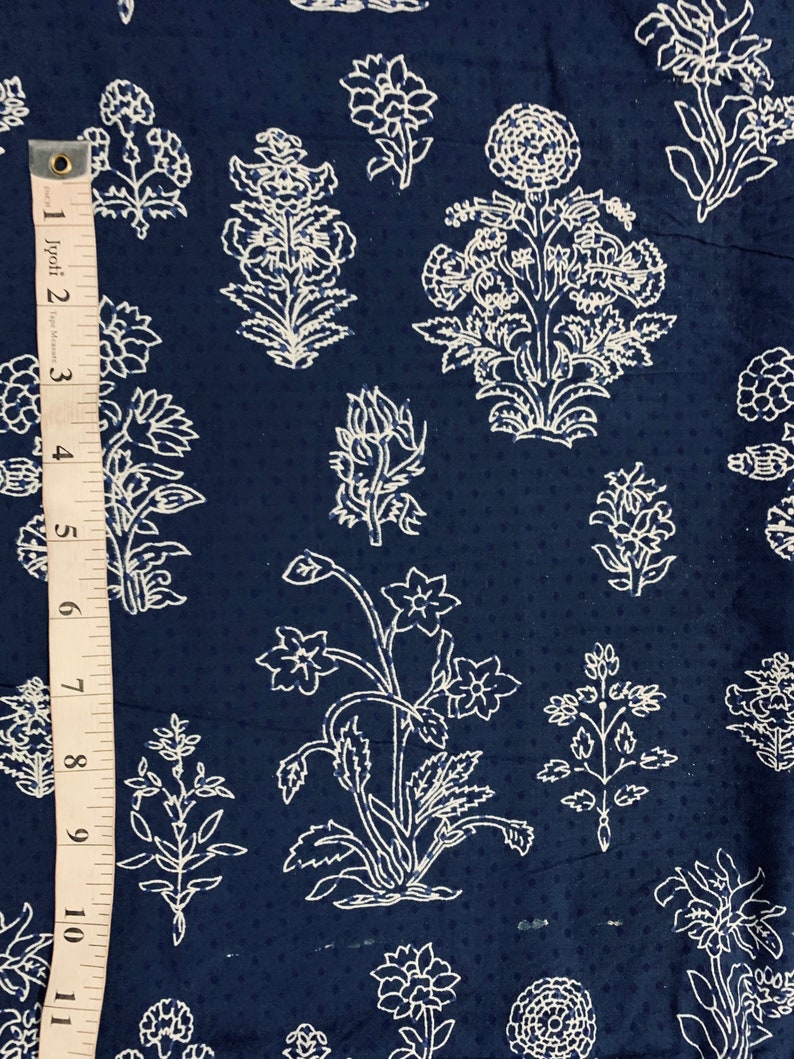 May include: A navy blue fabric with a white floral pattern. The fabric has a subtle dotted texture. The pattern features various floral motifs, including large and small flowers, leaves, and stems.
