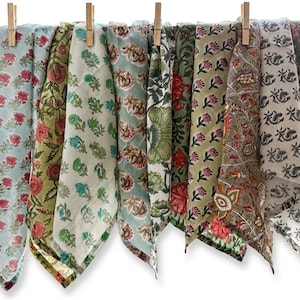 May include: A collection of colorful floral patterned fabric squares hanging from a white rod with wooden clothespins. The fabrics feature various designs in shades of blue, green, red, and brown.