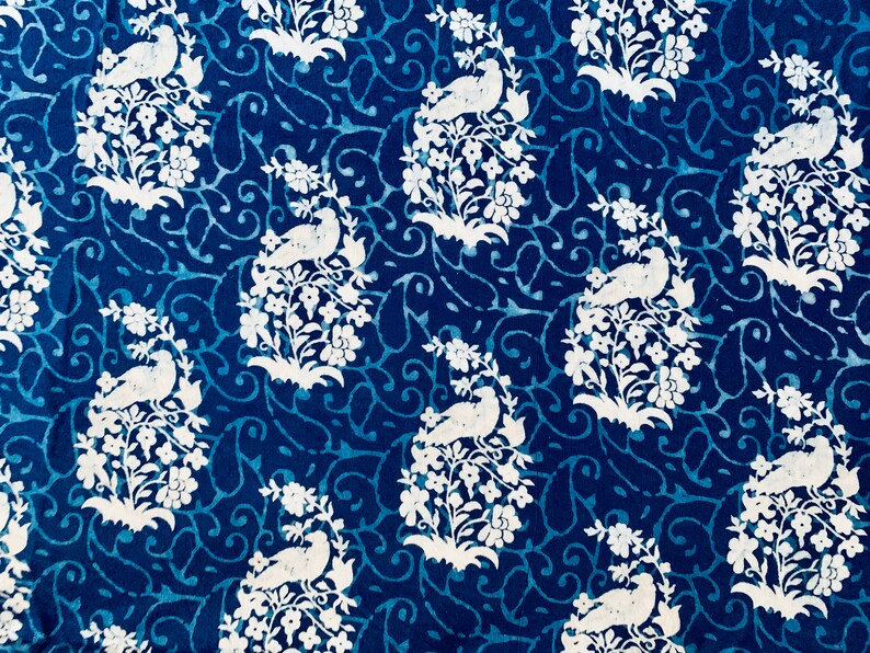 May include: A blue fabric with a white repeating pattern of birds perched on branches with flowers. The pattern is a traditional design.