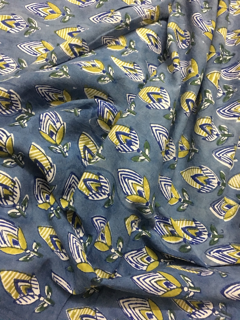 May include: Blue fabric with a repeating pattern of yellow, white, and blue stylized flowers. The fabric has a slightly textured surface.