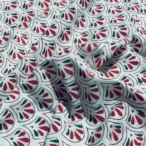 May include: White fabric with a repeating pattern of stylized red and green fan-like shapes. The fabric is slightly wrinkled, suggesting it is a soft material, and the pattern is evenly distributed across the surface.
