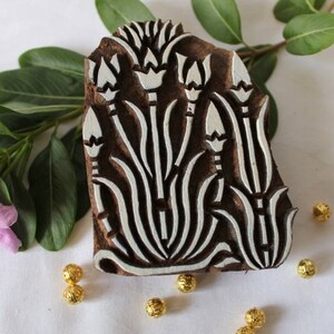 May include: A wooden printing block with a white floral design. The block is carved with a pattern of stylized flowers and leaves. The block is brown and has a natural wood finish.