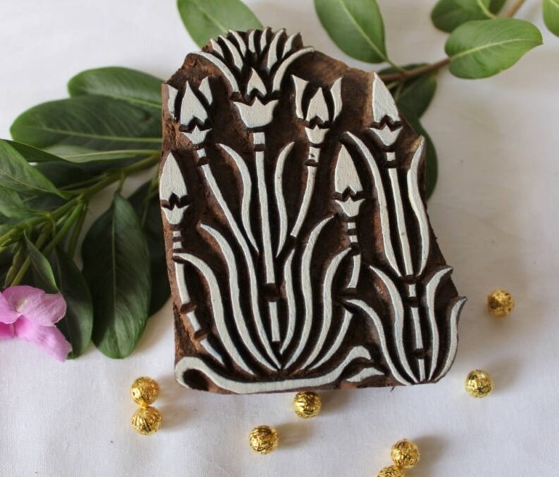 May include: A wooden printing block with a white floral design. The block is carved with a pattern of stylized flowers and leaves. The block is brown and has a natural wood finish.