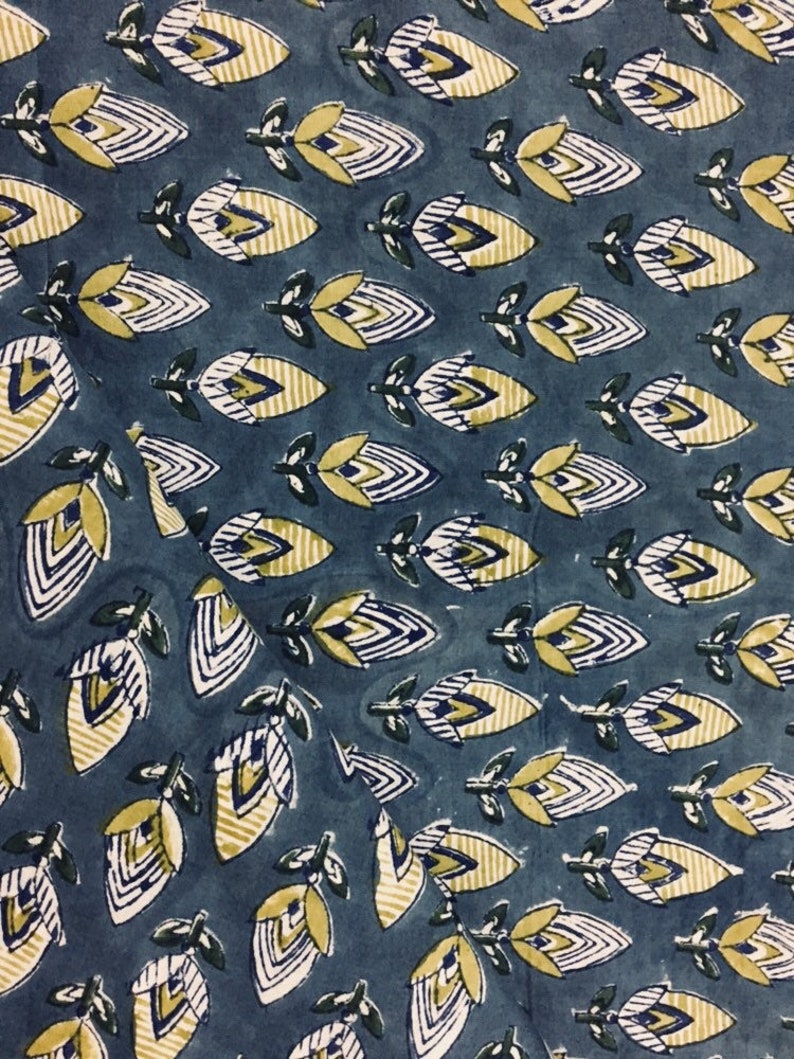 May include: Blue fabric with a repeating pattern of yellow and white stylized flowers. The flowers have a geometric design with white lines and yellow accents.
