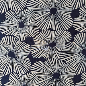 May include: Close-up of a fabric with a repeating pattern of white, stylized flower-like shapes against a dark navy blue background. The design features radial lines emanating from a central dark circle.