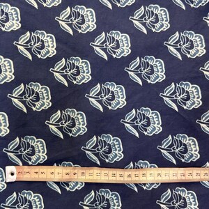 May include: A navy blue fabric with a white and light blue floral pattern. The fabric is shown with a measuring tape.