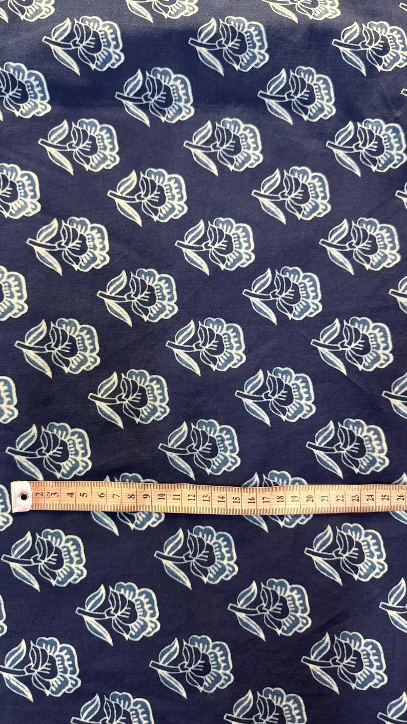 May include: A navy blue fabric with a white and light blue floral pattern. The fabric is shown with a measuring tape.