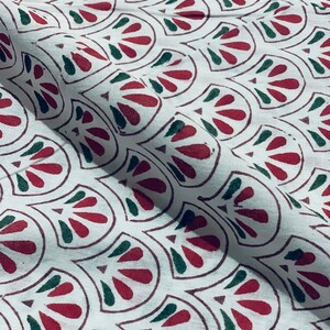 May include: White fabric with a repeating pattern of red and green stylized leaf shapes. The leaves are outlined in a dark red-brown color. The fabric is folded, showing the texture and drape of the material.