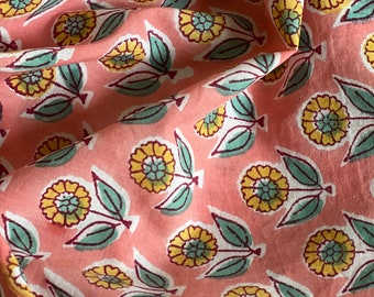 Op de afbeelding: Roze stof met een herhalend patroon van gele en groene bloemenmotieven. De stof heeft een zachte, textuur.