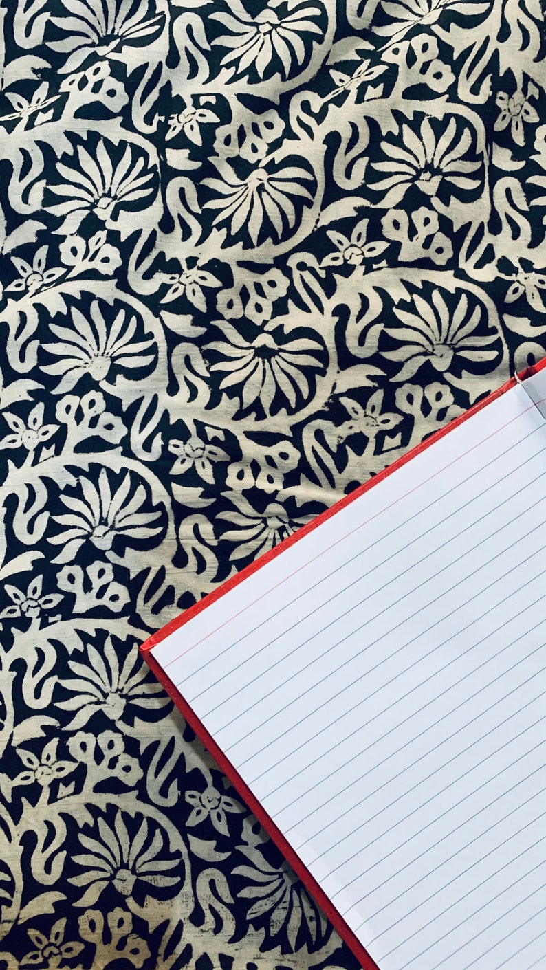 May include: A red notebook with lined pages is lying open on a black and white fabric with a floral pattern.