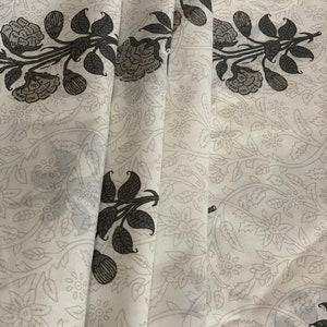 May include: White fabric with a black floral pattern. The fabric has a subtle sheen and a soft texture.