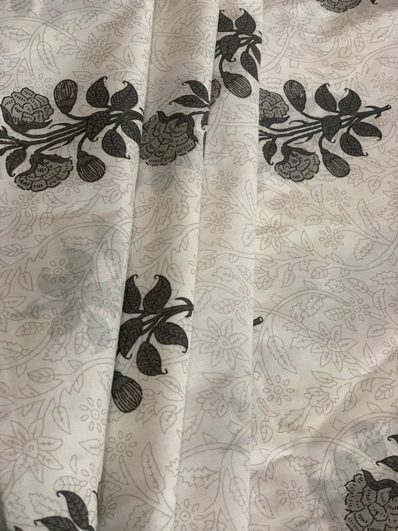 May include: White fabric with a black floral pattern. The fabric has a subtle sheen and a soft texture.