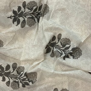May include: White fabric with a repeating pattern of black floral designs. The fabric has a soft, flowing texture.
