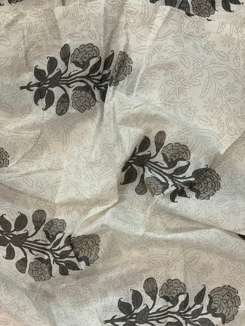May include: White fabric with a repeating pattern of black floral designs. The fabric has a soft, flowing texture.