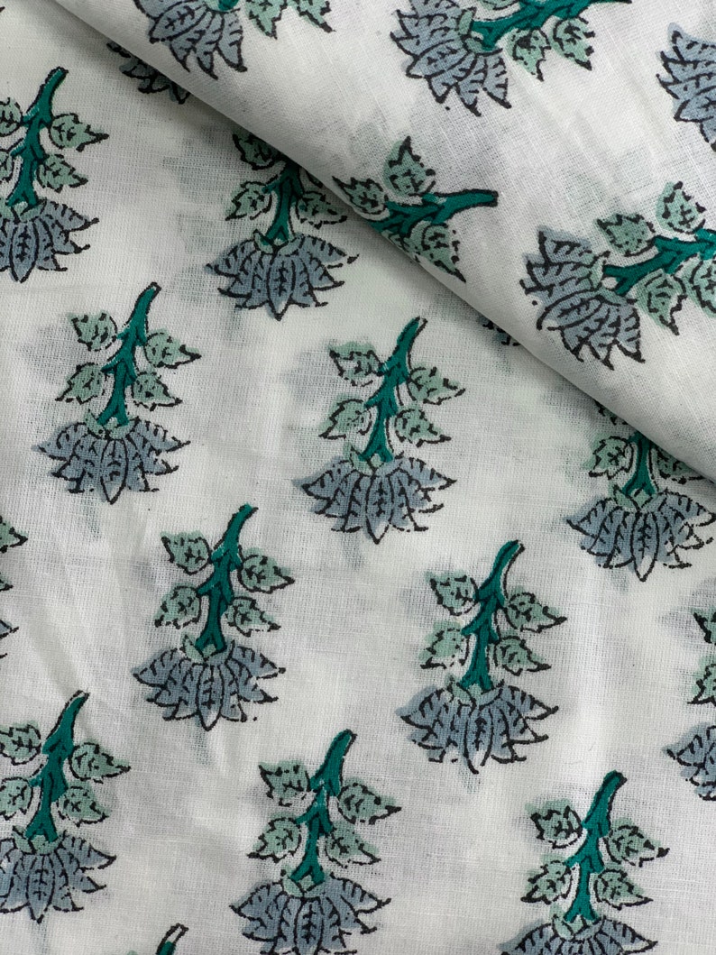 May include: White fabric with a repeating pattern of teal green and grey floral designs. The fabric has a soft, textured look.
