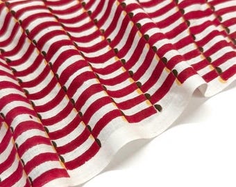 May include: A piece of white fabric featuring a repeating pattern of wavy, bold red stripes. Each red stripe is accented with a series of small, dark brown semi-circular shapes along one edge, creating a rhythmic, textured visual effect across the textile.