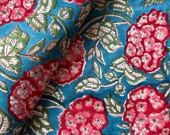 May include: Close-up of a fabric with a floral pattern. The design features large, clustered red flowers with pink accents and green leaves on a teal blue background. The fabric is folded.