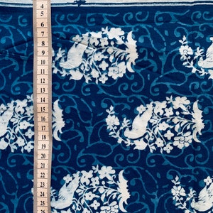 May include: Blue cotton fabric with a white floral and bird pattern. The fabric is measured with a ruler in inches.