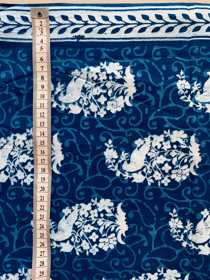 May include: Blue cotton fabric with a white floral and bird pattern. The fabric is measured with a ruler in inches.