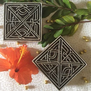 May include: Two wooden printing blocks with intricate geometric designs. The blocks are black and white and have a square and diamond shape.