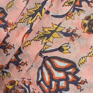 May include: Pink fabric with a floral print featuring yellow, orange, and gray flowers. The fabric has a subtle watercolor effect.