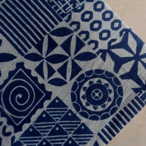 May include: A white fabric with a blue indigo pattern of various geometric shapes, including circles, squares, and stars. The fabric has a textured surface.