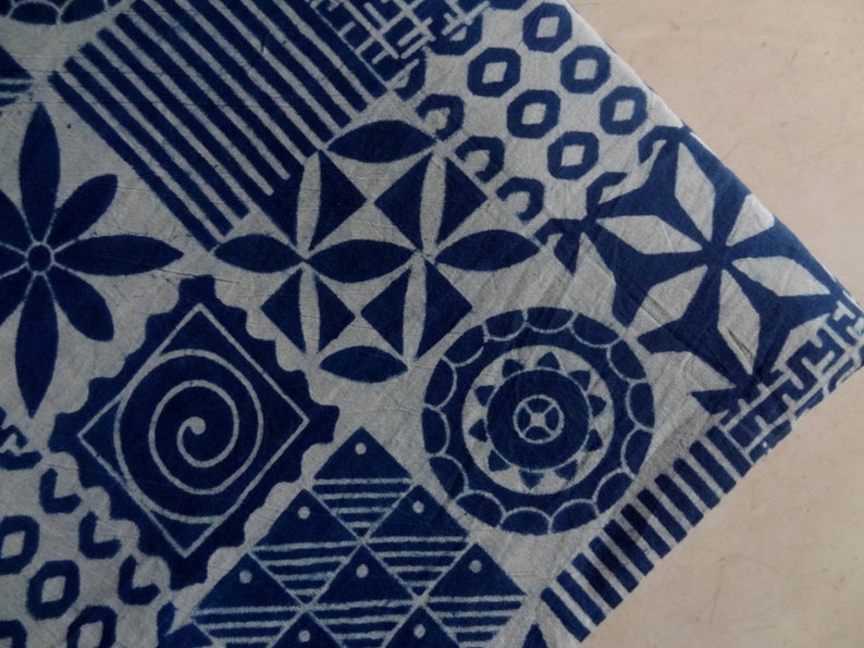 May include: A white fabric with a blue indigo pattern of various geometric shapes, including circles, squares, and stars. The fabric has a textured surface.