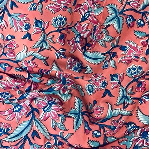 May include: A pink fabric with a floral pattern in shades of blue, pink, and white. The fabric has a wrinkled texture and a repeating pattern of flowers and leaves.