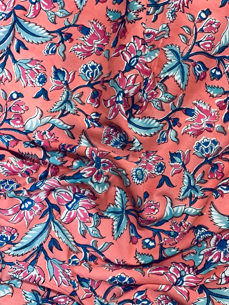 May include: A pink fabric with a floral pattern in shades of blue, pink, and white. The fabric has a wrinkled texture and a repeating pattern of flowers and leaves.