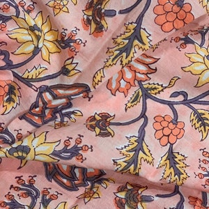 May include: A pink fabric with a floral pattern. The flowers are in shades of orange, yellow, and white. The fabric has a vintage feel.