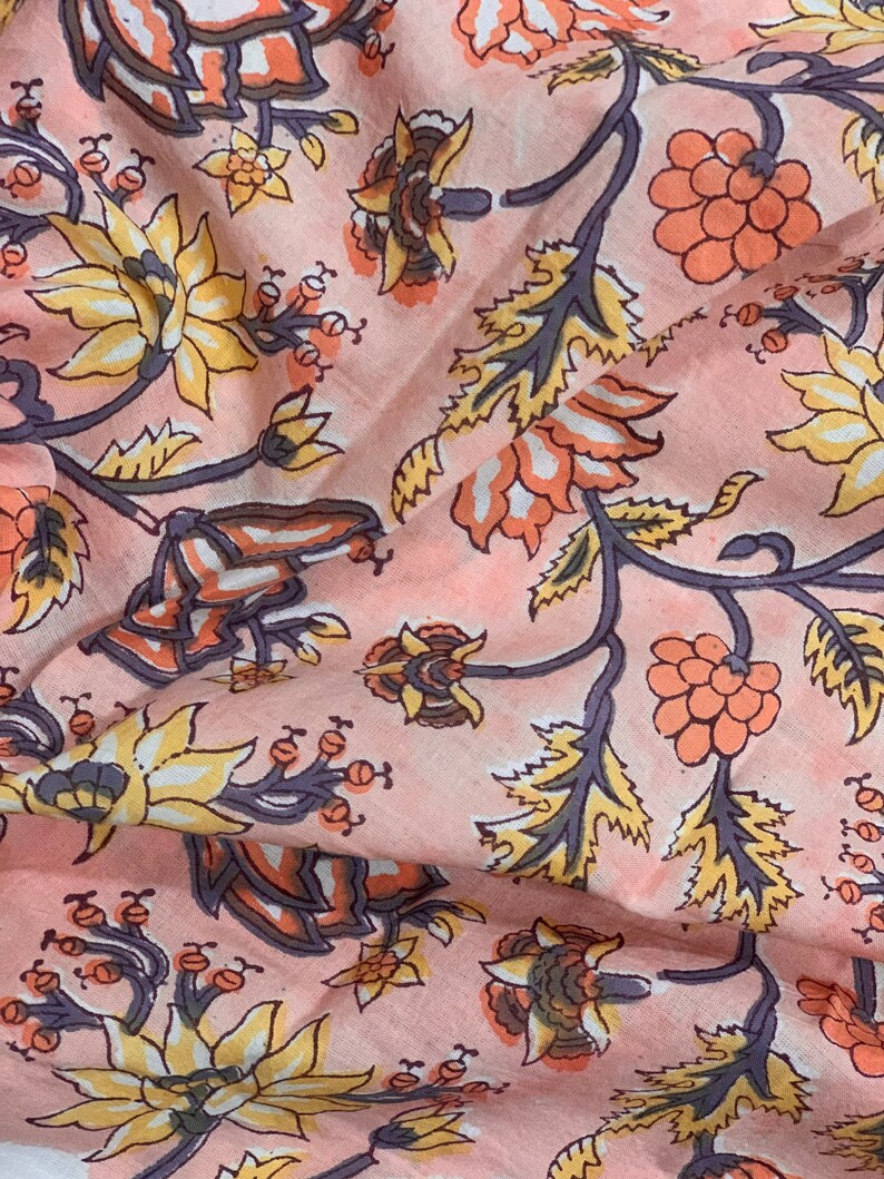 May include: A pink fabric with a floral pattern. The flowers are in shades of orange, yellow, and white. The fabric has a vintage feel.