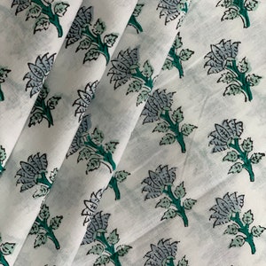 May include: White cotton fabric with a repeating pattern of blue and green floral designs. The fabric is folded in a few places, showing the pattern from different angles.