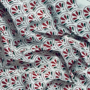 May include: White fabric with a repeating pattern of stylized red and green fan-shaped designs. The fabric has a slightly wrinkled texture, suggesting it is a soft material like cotton or linen. The pattern is outlined in a dark brown color.