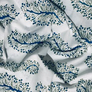 May include: White fabric with a repeating pattern of blue and green stylized tree branches. The fabric is folded and wrinkled.