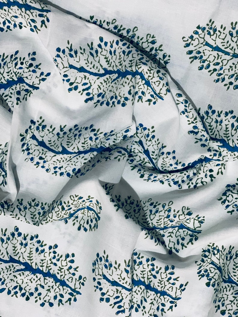 May include: White fabric with a repeating pattern of blue and green stylized tree branches. The fabric is folded and wrinkled.
