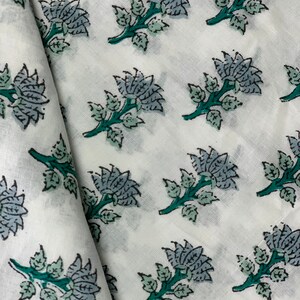 May include: White fabric with a repeating pattern of blue and green floral designs. The flowers are stylised and have a vintage look.