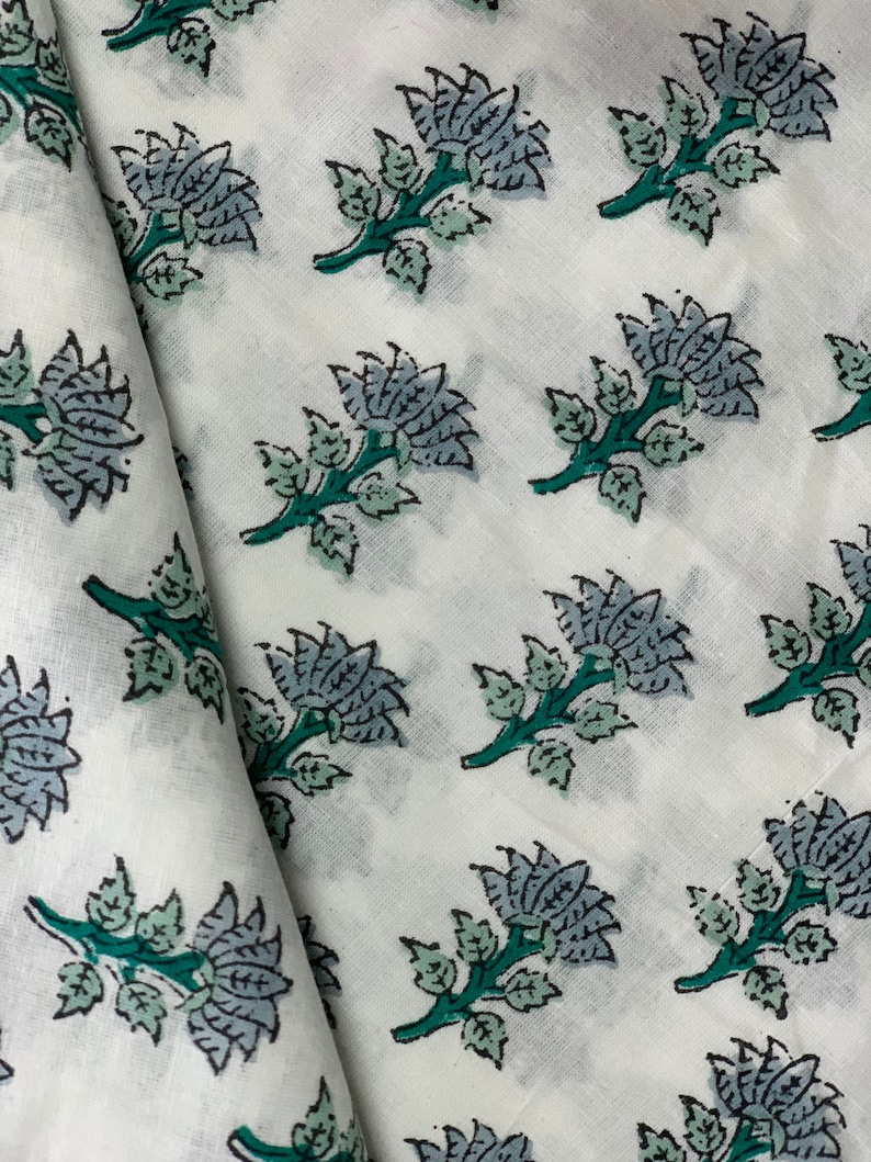 May include: White fabric with a repeating pattern of blue and green floral designs. The flowers are stylised and have a vintage look.