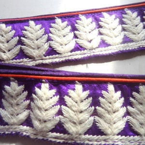 May include: Purple fabric trim with white embroidered leaves and a red stripe along the edge.