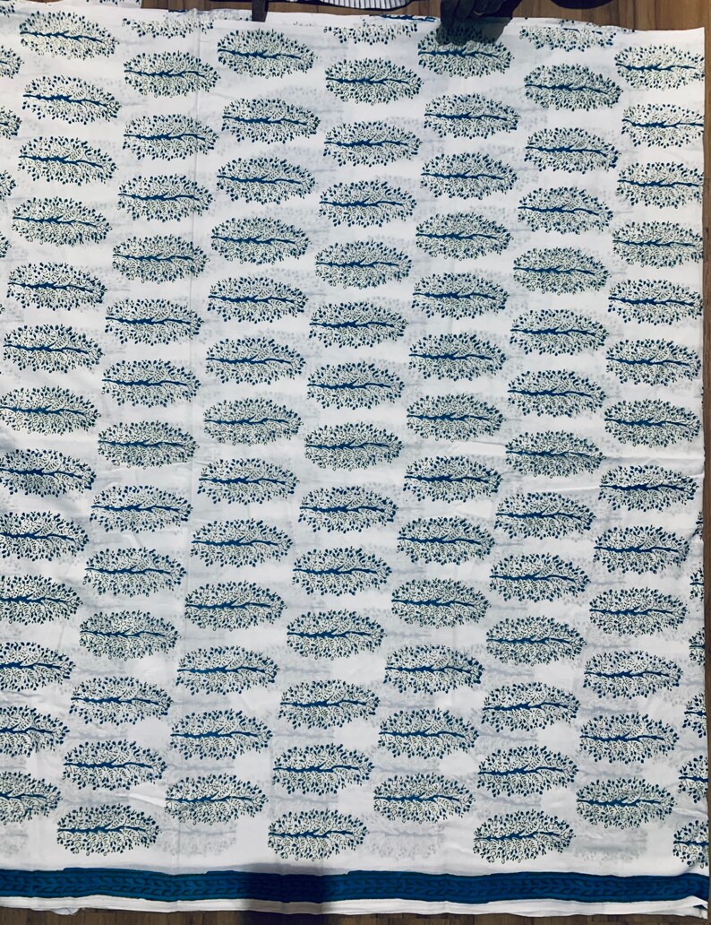 May include: White fabric with a repeating pattern of blue and green stylized tree branches in an oval shape.