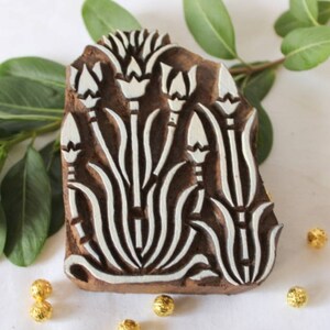 May include: A wooden printing block with a floral design. The block is carved with a pattern of stylized flowers and leaves. The design is in white against a brown background.