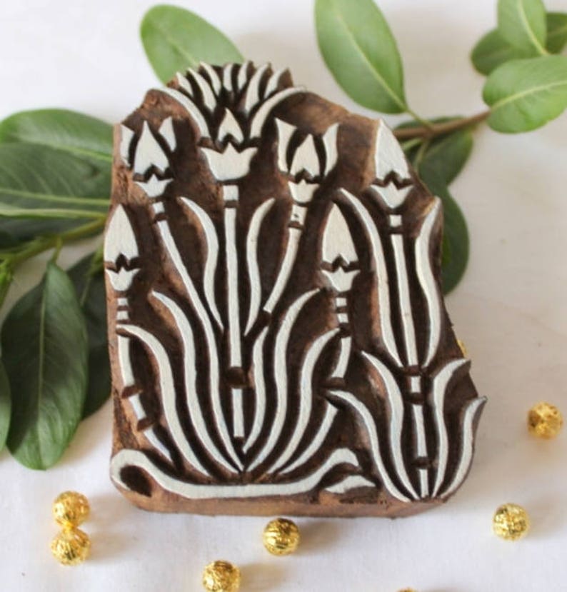 May include: A wooden printing block with a floral design. The block is carved with a pattern of stylized flowers and leaves. The design is in white against a brown background.
