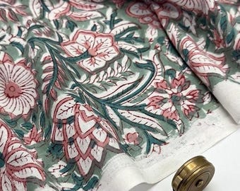 Op de afbeelding: Een gevouwen stuk stof met een bloemenpatroon in tinten oudroze, saliegroen en wit. Een messing meetlint toont een lengte van 12,7 cm en een messing schaar ligt naast de stof op een witte ondergrond.