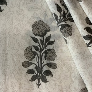 May include: White fabric with a black floral pattern. The fabric features a repeating design of stylized flowers and leaves.