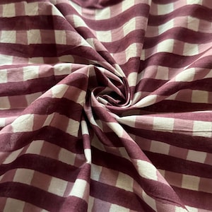 May include: A close-up of a pink and white gingham fabric. The fabric is folded and has a soft, textured appearance.