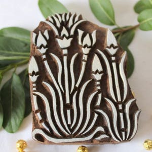 May include: A wooden printing block with a floral design. The block is carved with a pattern of white flowers and leaves on a brown background.