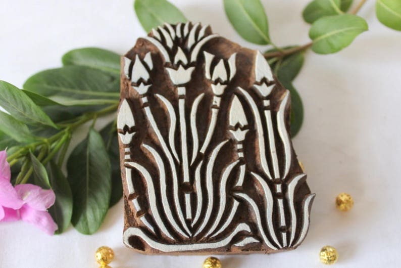May include: A wooden printing block with a floral design. The block is carved with a pattern of white flowers and leaves on a brown background.