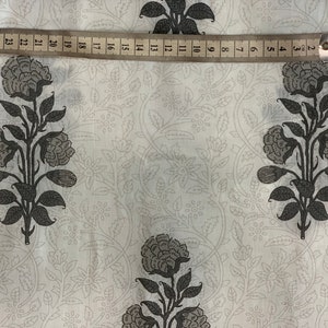 May include: White fabric with a repeating pattern of black floral designs. The fabric is measured with a ruler that shows inches.